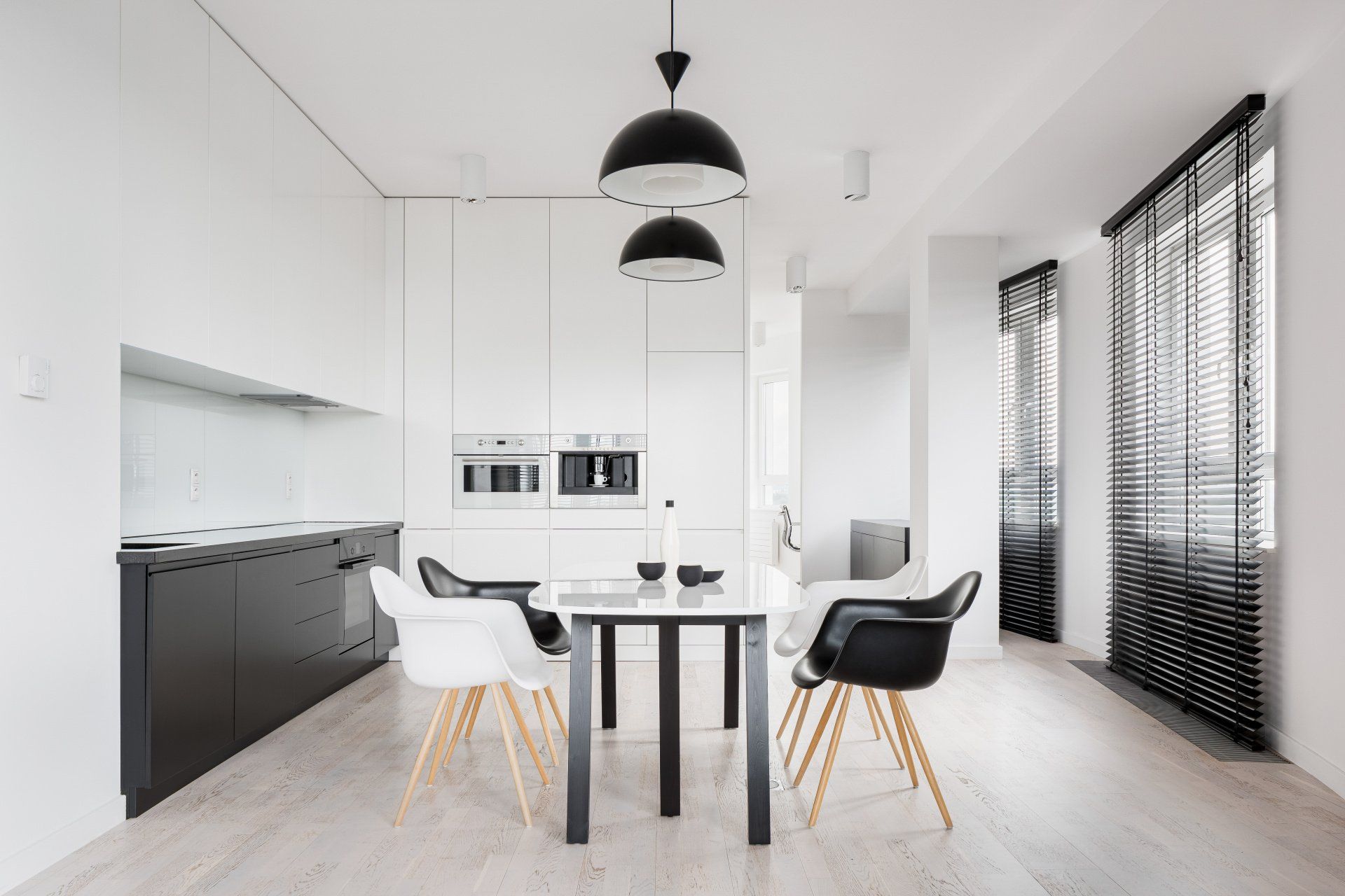 Modern kitchen and dining room with black and white decor. Table with four chairs beneath pendant lights.