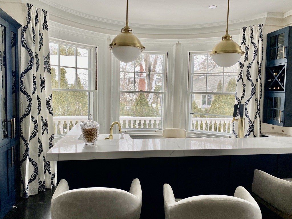 Bright kitchen with marble island, pendant lights, and large windows framed by patterned curtains