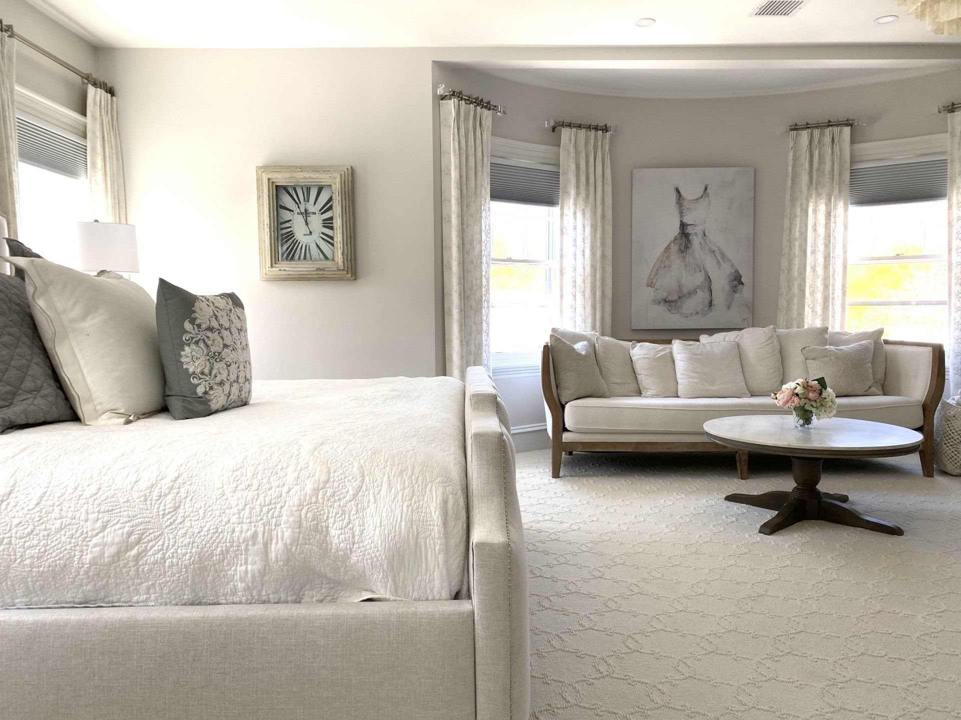 Bedroom with a white bed, sofa, and round coffee table on a white carpet, and decorative curtains.