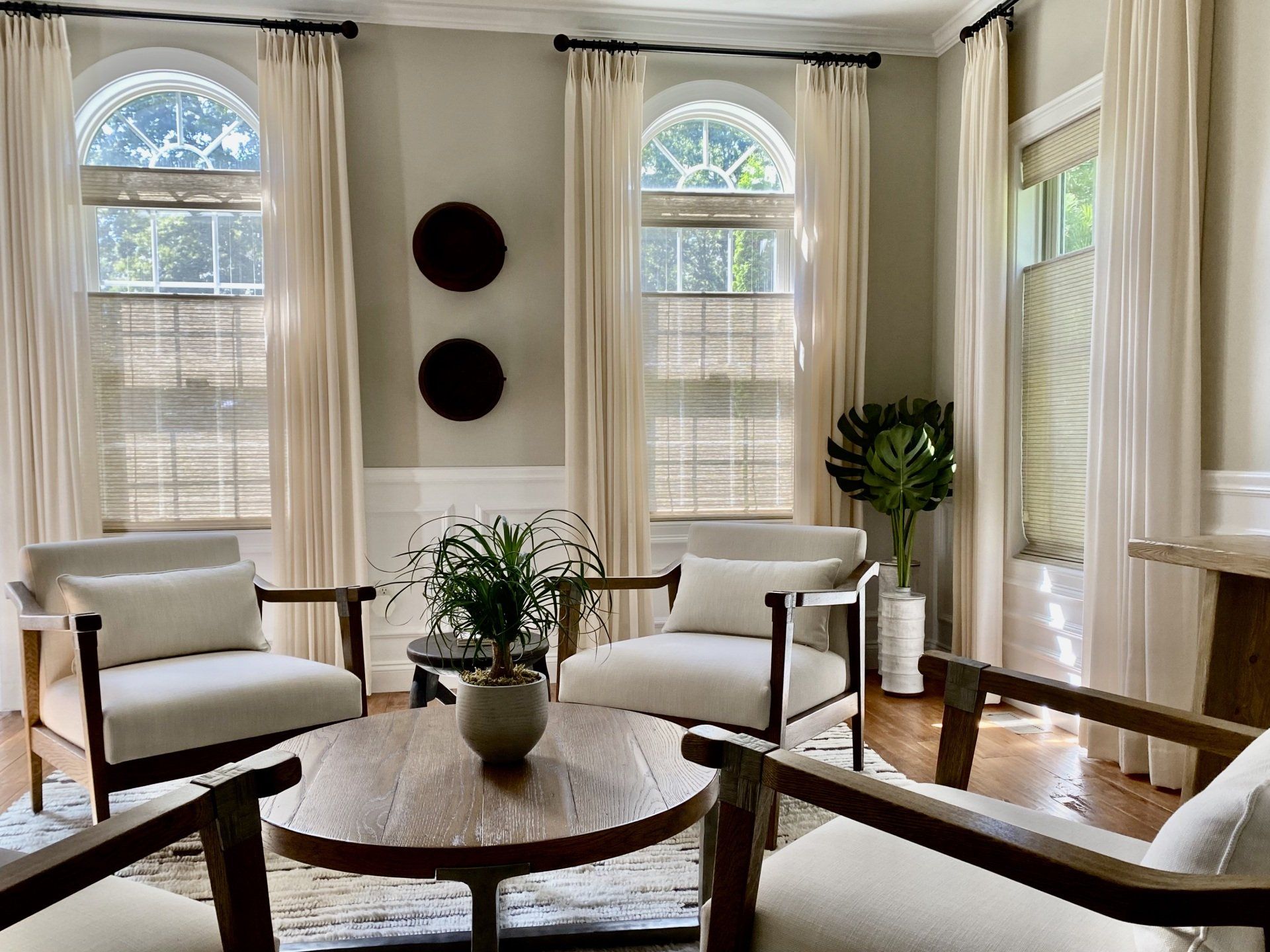 Living room with four white armchairs, a round table, and arched windows with curtains.