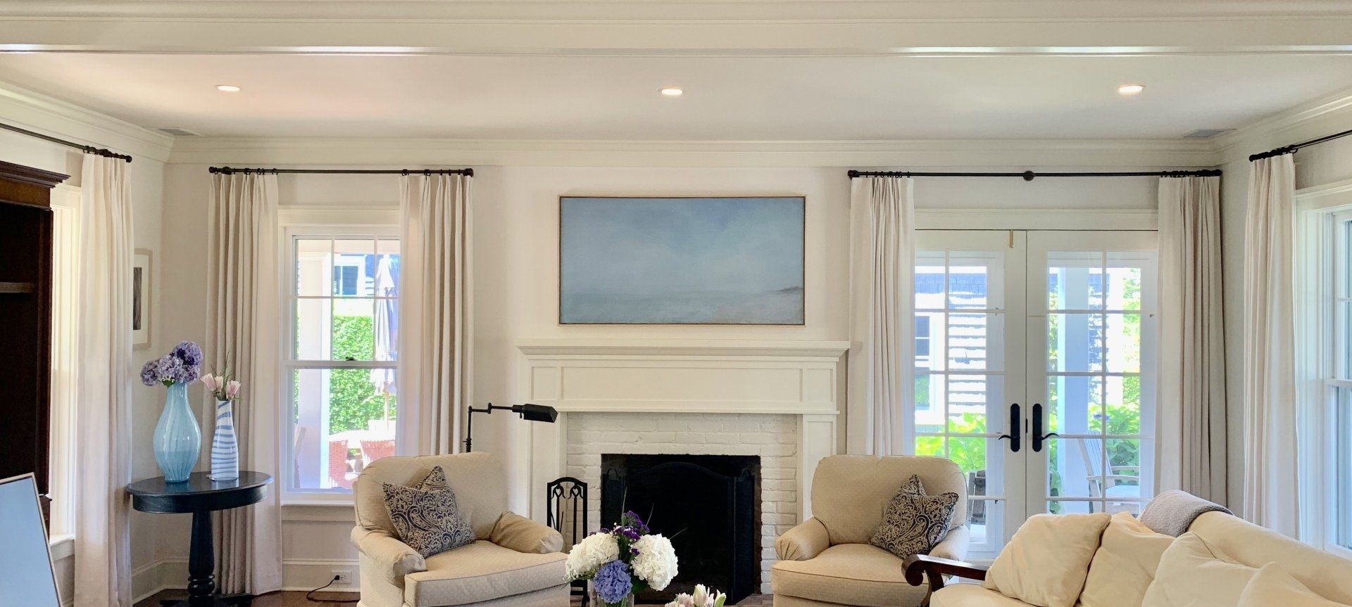 A living room with a fireplace, chairs, and windows with curtains.