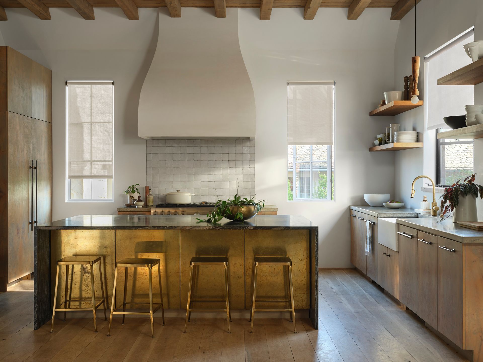 Modern kitchen with brass island, light wood cabinets, and two windows with shades.