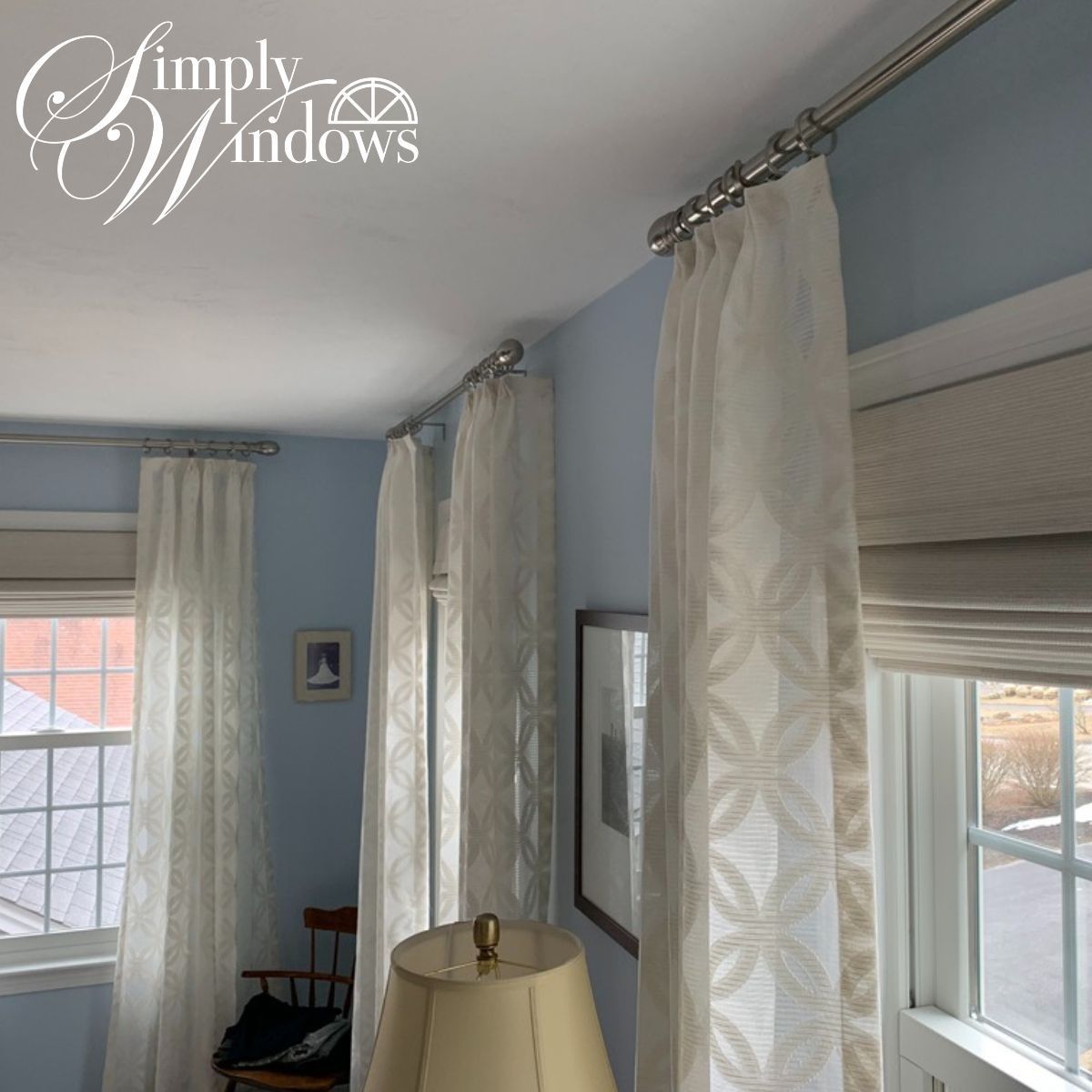 Bright bedroom with blue walls, white curtains, and a window with a Roman shade and decorative drapes.