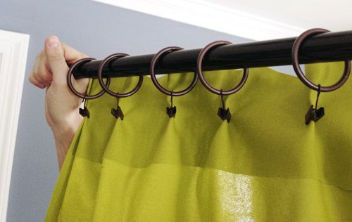 a person is hanging a green custom drapery on a black pole Simply Windows.