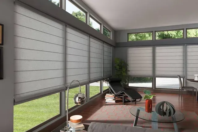 Modern living room with large windows, light gray Roman shades, and view of a green lawn.