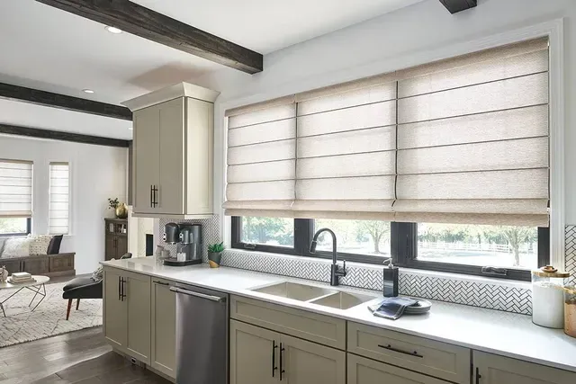 Kitchen with beige Roman shades, light cabinets, and a white countertop. Sink and faucet visible.