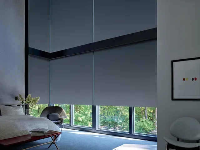 Bedroom interior with large windows, gray blinds, and a view of trees.