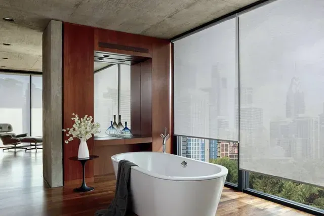 Bathroom with a white bathtub, floor-to-ceiling windows, and sheer white roller shades.