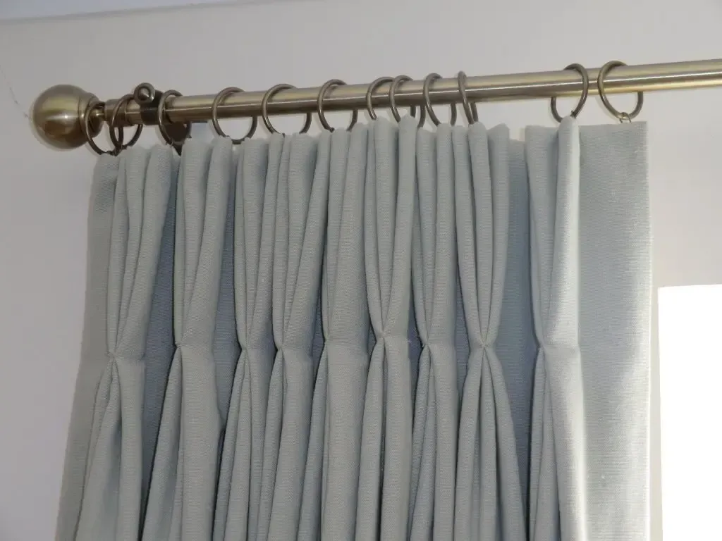 Light gray curtains hanging from a brass curtain rod with rings