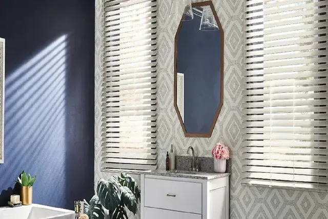 Bathroom interior with blue and patterned walls, white vanity, hexagon mirror, and blinds.