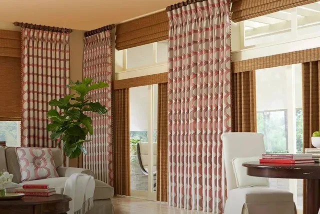Living room with patterned curtains, blinds, sofa, round table, and a plant.