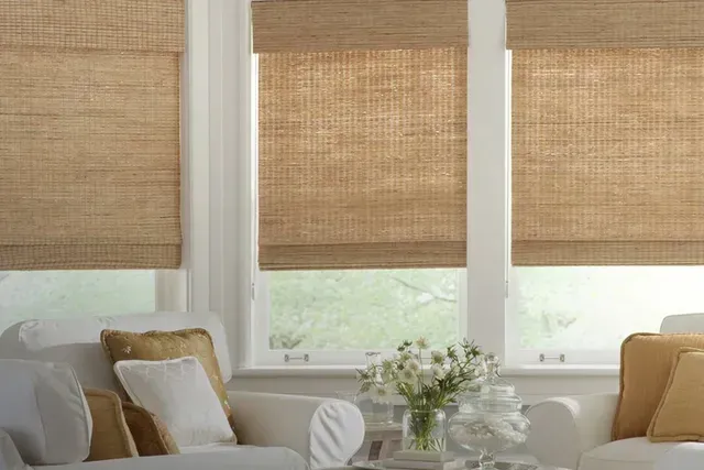 Three windows with woven, tan shades. A white couch with yellow and white pillows is visible.