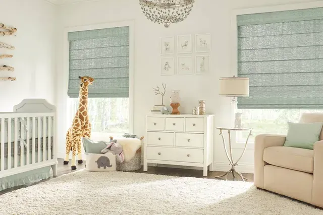 Baby's nursery with crib, dresser, chair, and giraffe toy. Blue-green shades on the windows, white walls.