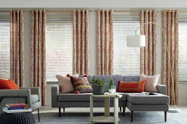 Living room with gray sofa, patterned curtains, white blinds, and arched lamp.