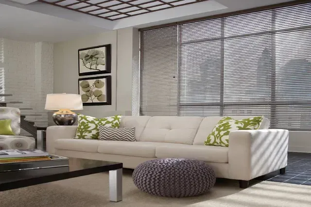 Living room with a white couch, patterned pillows, a black coffee table, and large window with blinds.