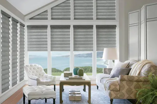 Living room with gray blinds, overlooking a seascape, furnished with white and patterned furniture.