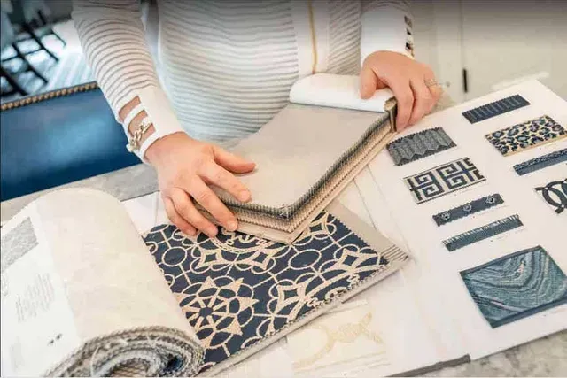 Person selecting fabric swatches, interior design samples, and patterned designs on a table.