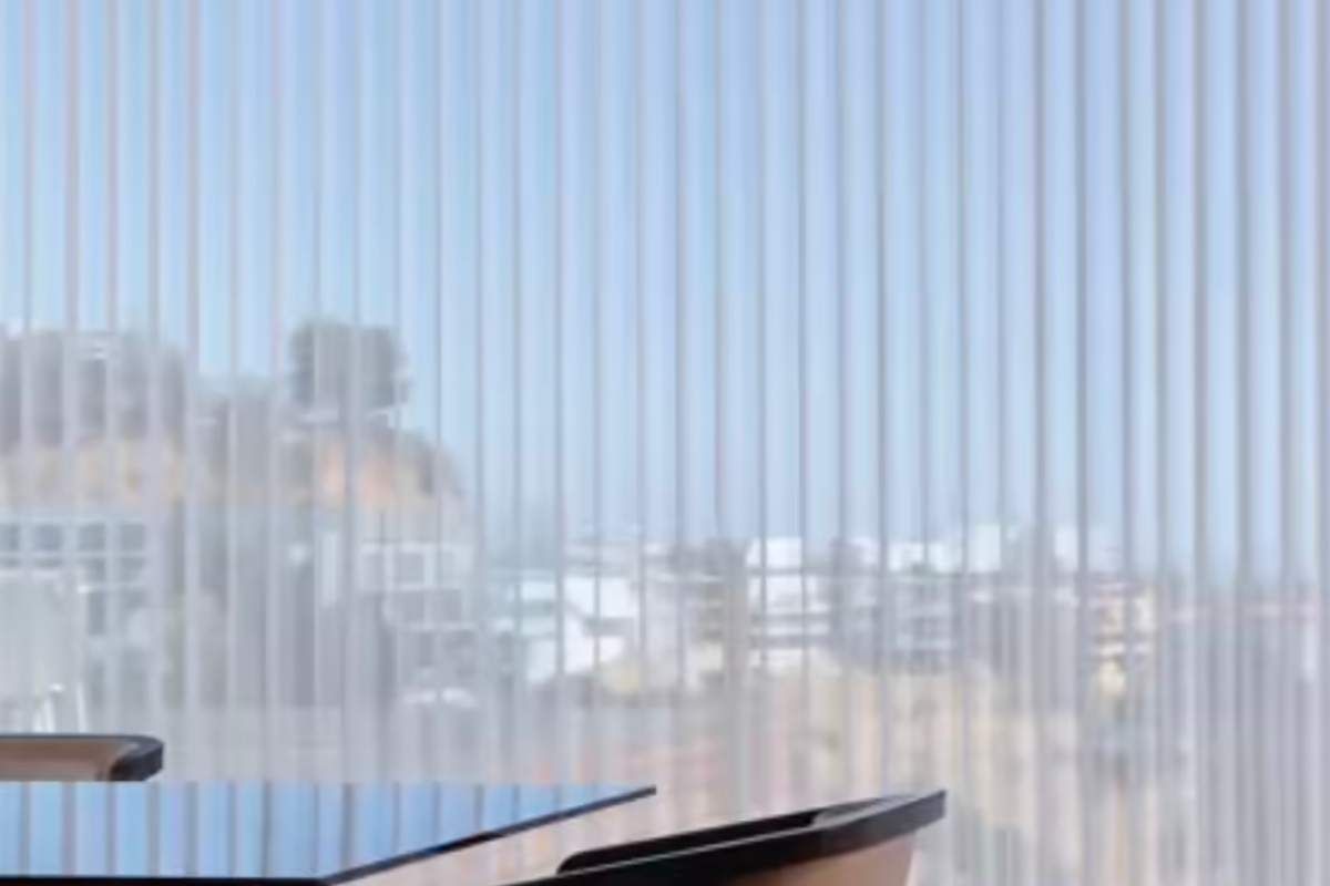 Vertical blinds in front of a window, with a blurred cityscape visible through the blinds.