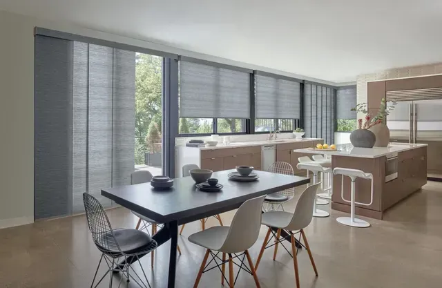 Modern kitchen and dining area with gray blinds, dark table, light chairs, and an island.
