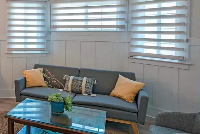 Living room with grey sofa, yellow pillows, blue coffee table, and striped window shades.