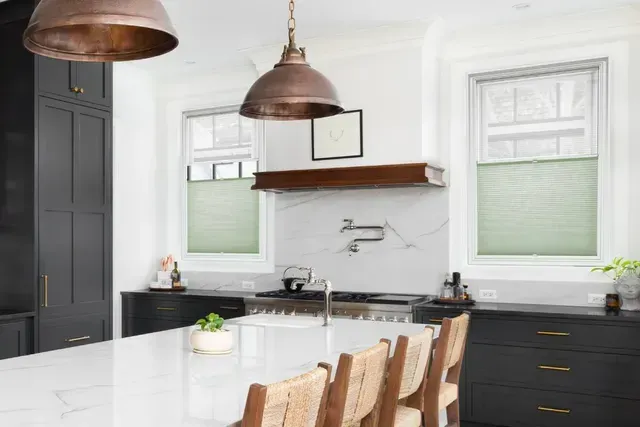 Kitchen with black cabinets, white island, copper pendant lights, and two windows.