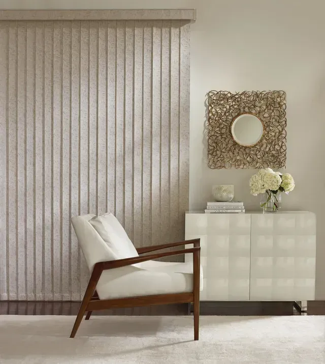 Beige vertical blinds, white chair, decorative mirror, and white cabinet in a neutral-toned room.