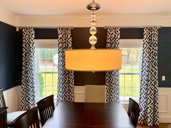 Dining room with dark blue walls, patterned curtains, and a large chandelier over a table.