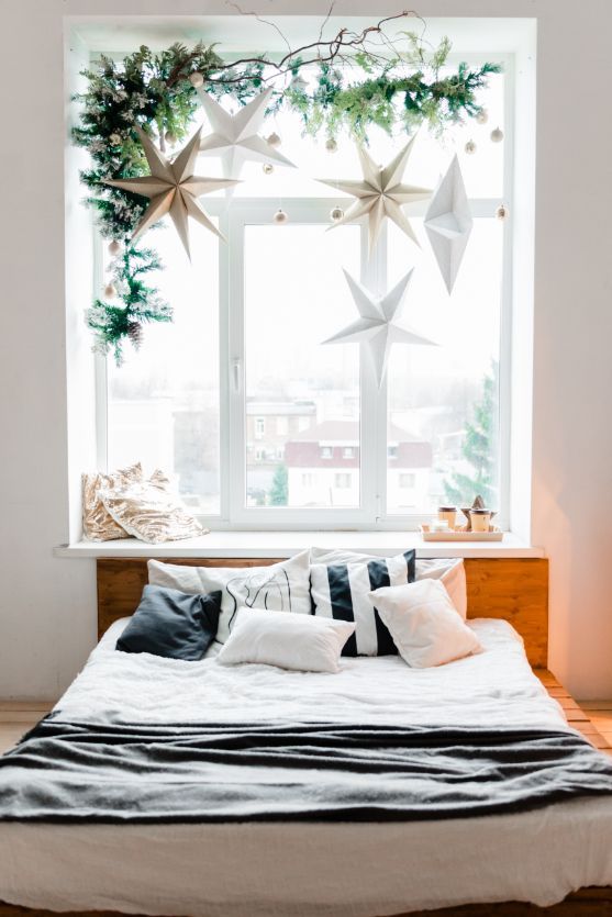 Bedroom with a bed, pillows, and a window decorated with stars and greenery.