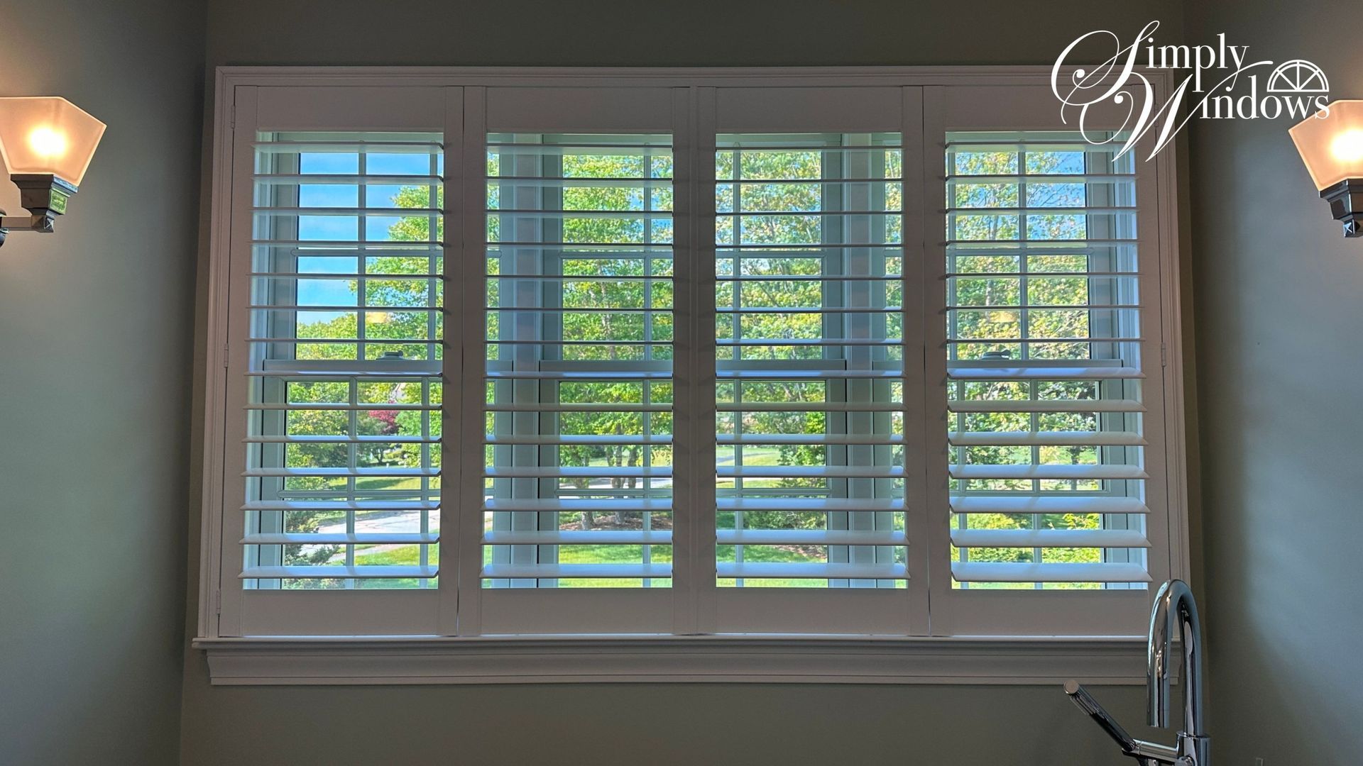 Living room window with white plantation shutters letting in daylight and greenery outside