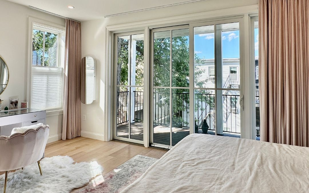 Bright bedroom with bed, vanity, rug, and large sliding glass doors to a balcony and city view
