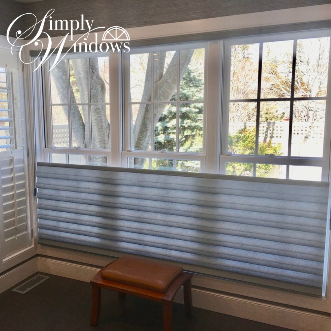 White cellular shade covering a large window above a small wooden bench in a bright room