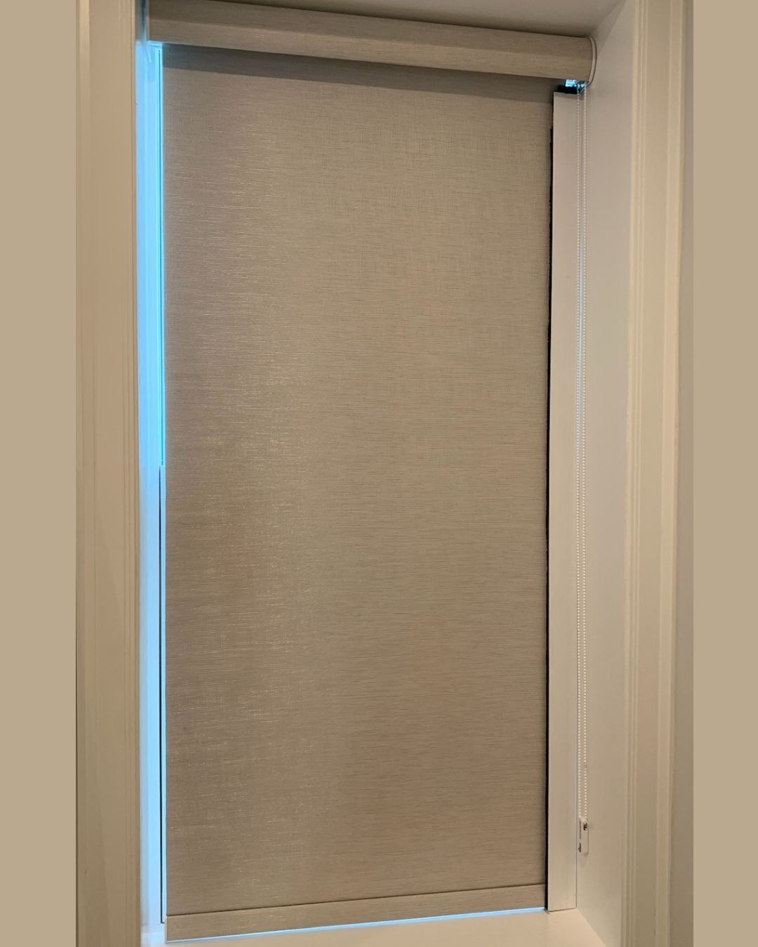 Beige roller shade inside a white window frame, partially covering a window.