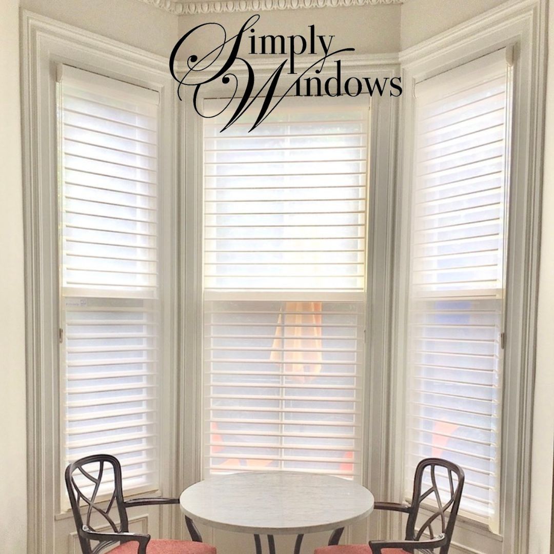 Bright white bay windows with Hunter Douglas silhouette shades and a small round table with two chairs.