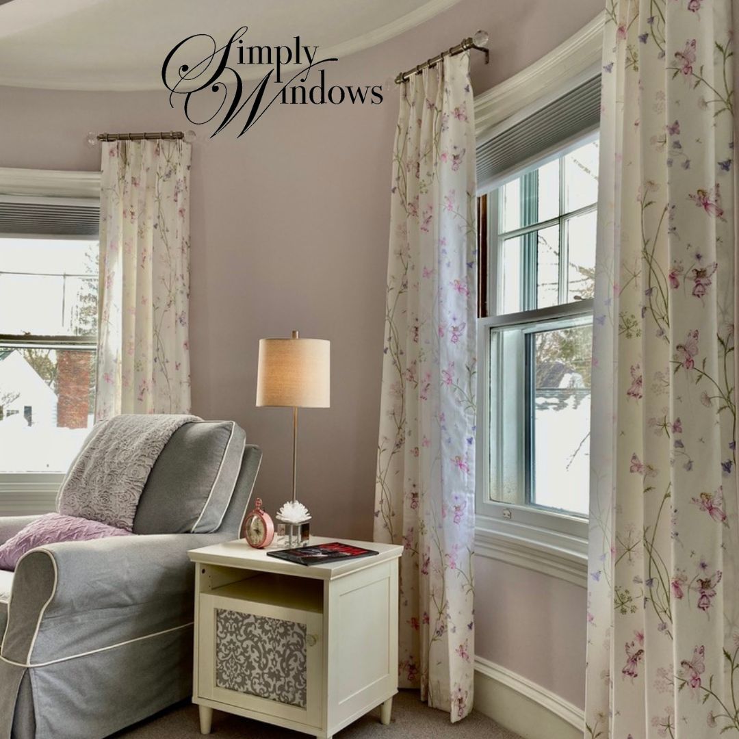 Bright bedroom nook with floral custom drapery, a window, a lamp, and a side table beside a gray chair.