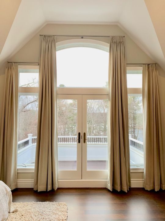 A large windowed wall with French doors highlights elegant drapery. 