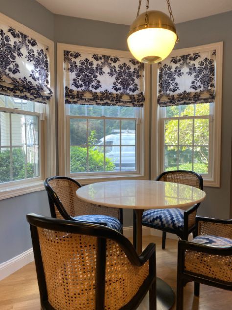 Dining nook with round table, four chairs, and blue and white patterned roman shades.