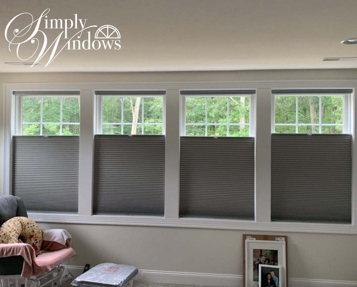 Cellular window shades cover four living room windows above a couch and framed photo.