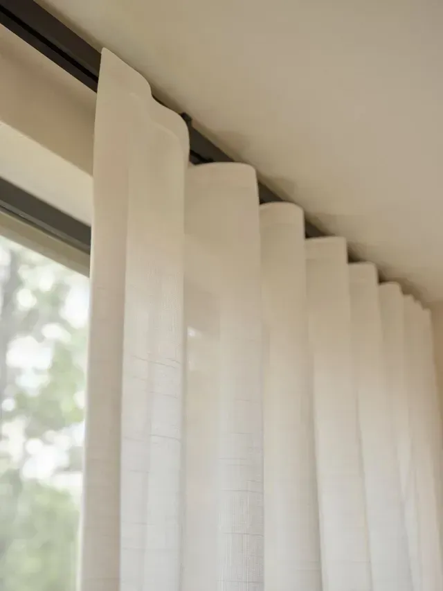 White sheer curtains hanging from a dark track in front of a window.