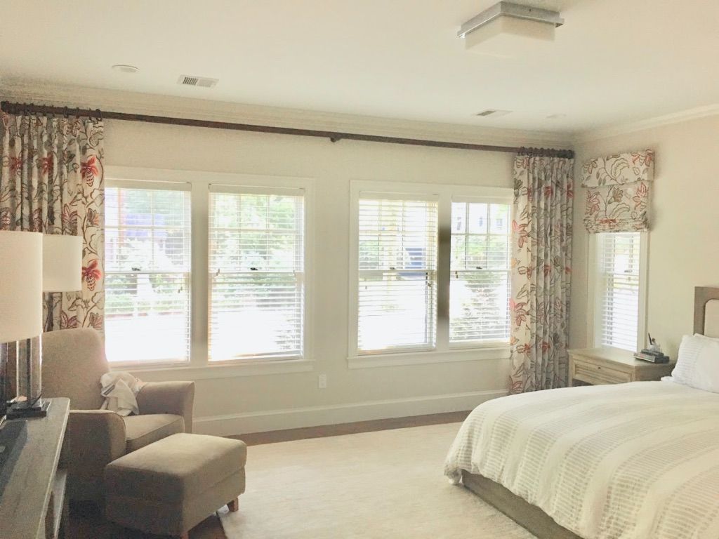 Bedroom with windows, floral curtains, bed, chair, and neutral tones.