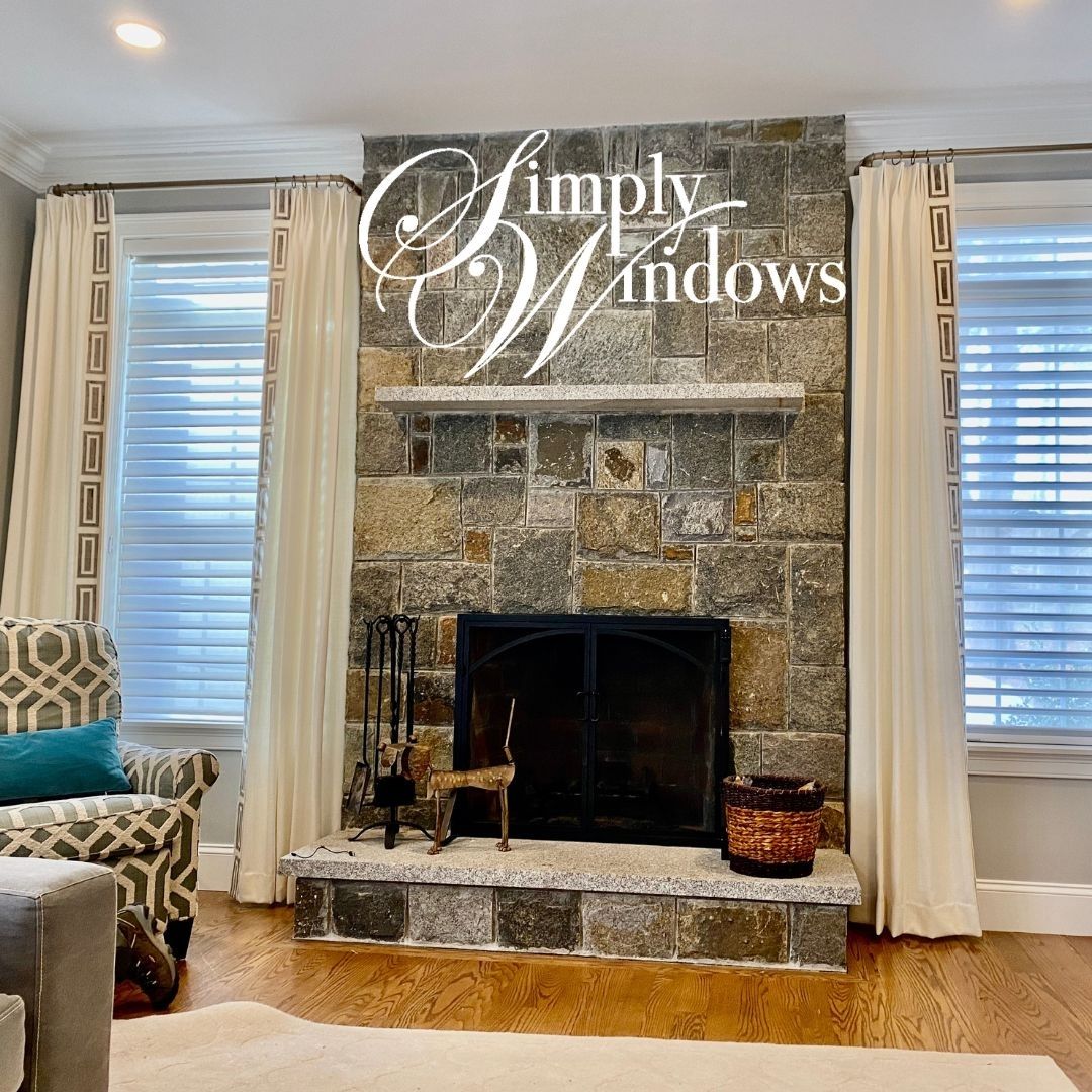Stone fireplace with white curtains and logo text “Simply Windows” in a living room.