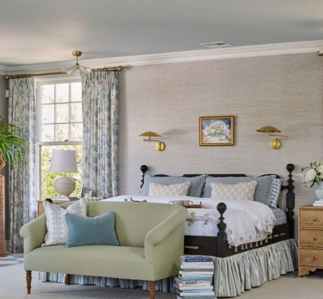 Bedroom with a green loveseat, floral curtains, a four-poster bed, and gold wall sconces.