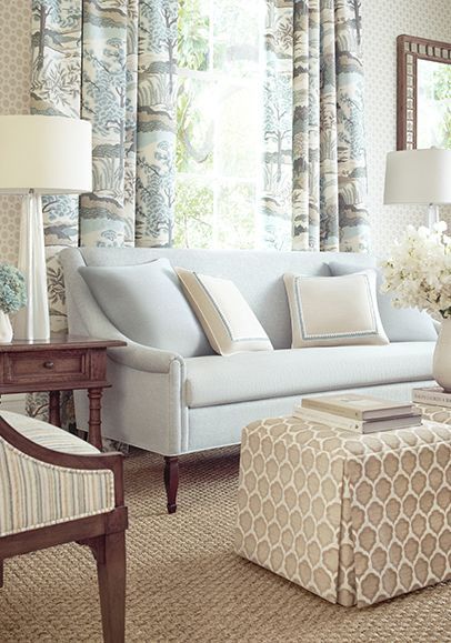 Living room with light blue sofa, floral curtains, patterned ottoman, and table lamp.