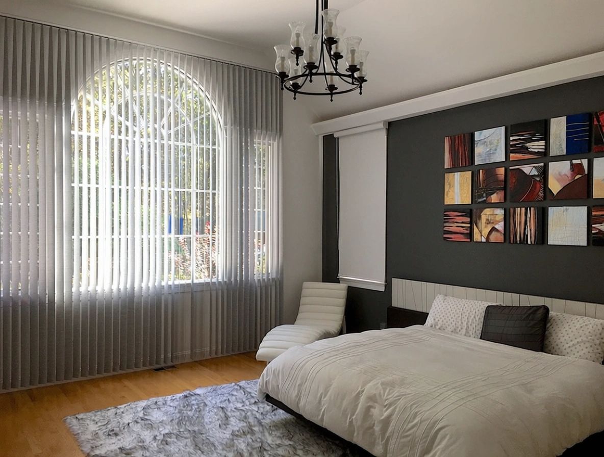 Bedroom with arched window, sheer curtains, bed, artwork, rug, and a chandelier.