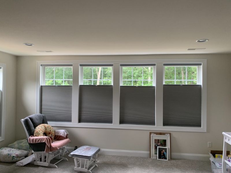 Room with large windows, gray blinds, a rocking chair, dog, and various decorative items.