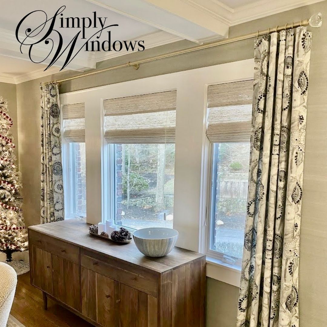 Living room window with patterned drapes, woven shades, and a wooden console table beneath.