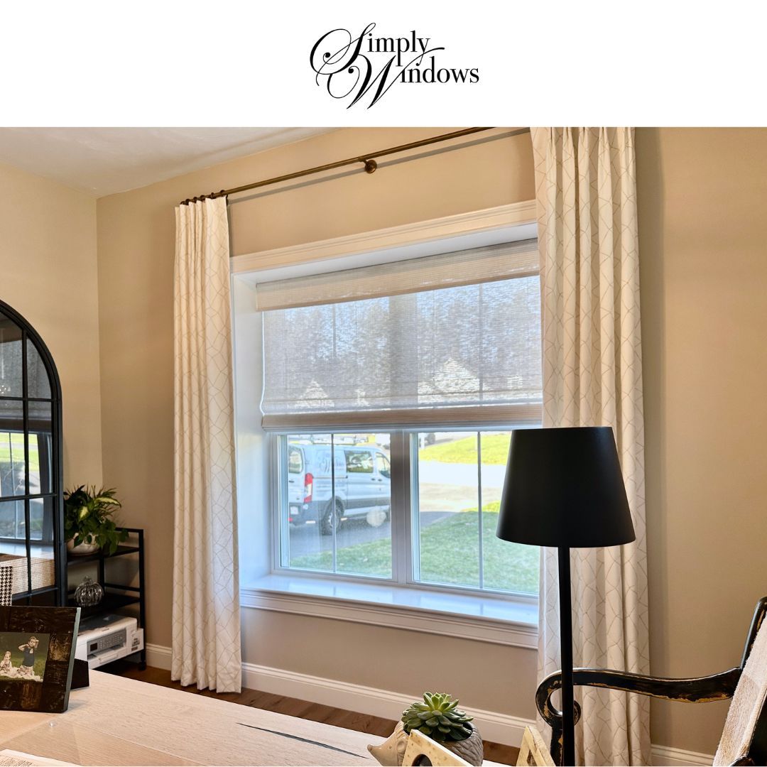 Bright living room with cream drapes, a large window, woven wood shades, and white upholstered chair