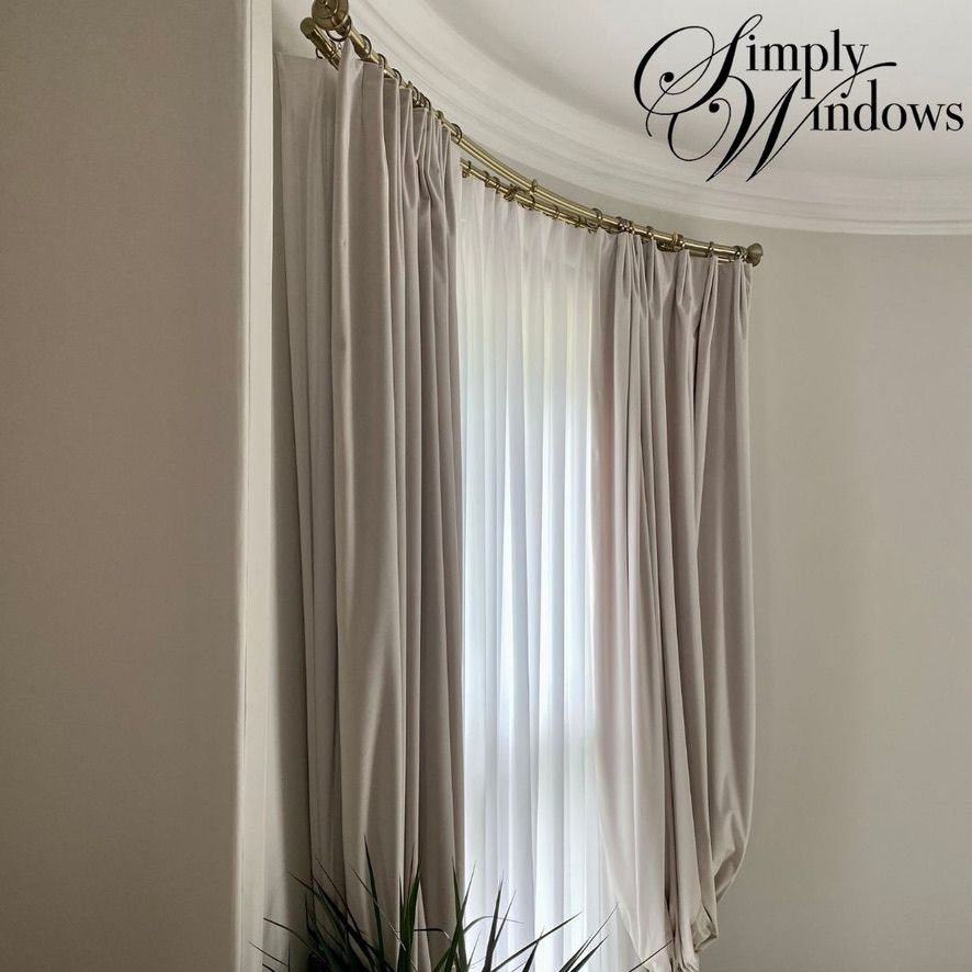 Floor-length taupe curtains framing a bright bay window in a light-colored room