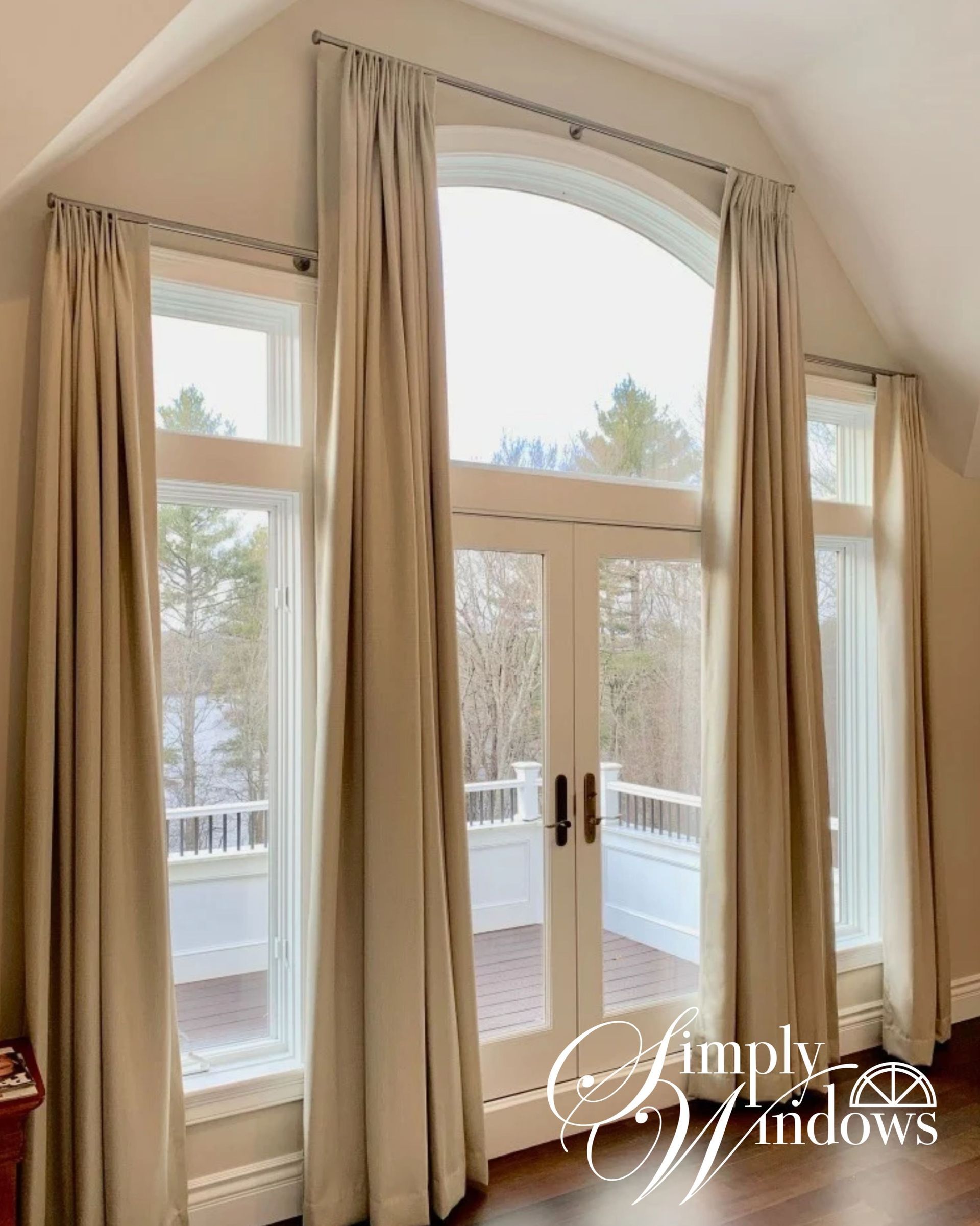 Tall arched windows with beige drapery overlooking a bright outdoor deck and trees