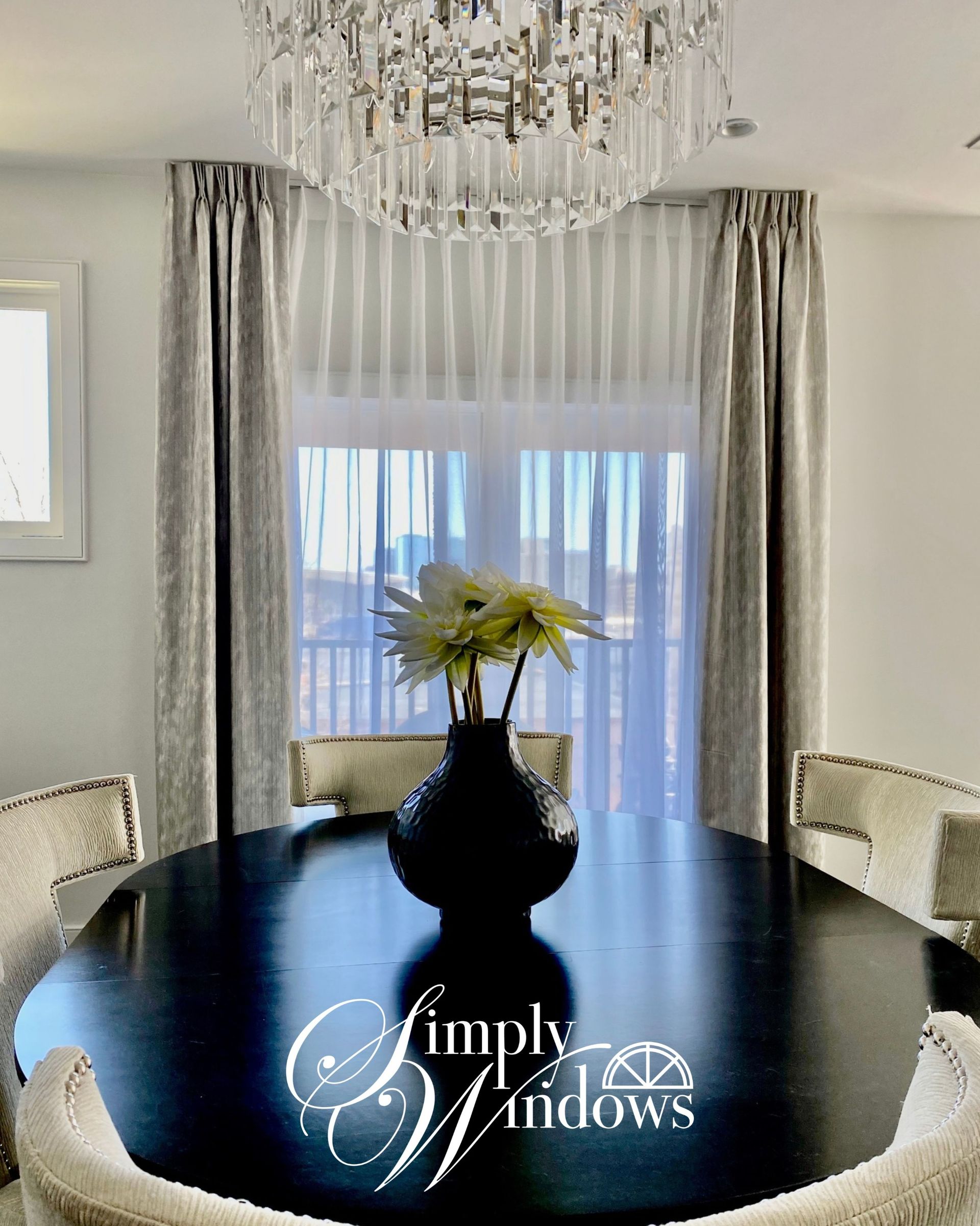 Elegant dining room with black table, chandelier, silver curtains, and window valance against sliding glass doors. 