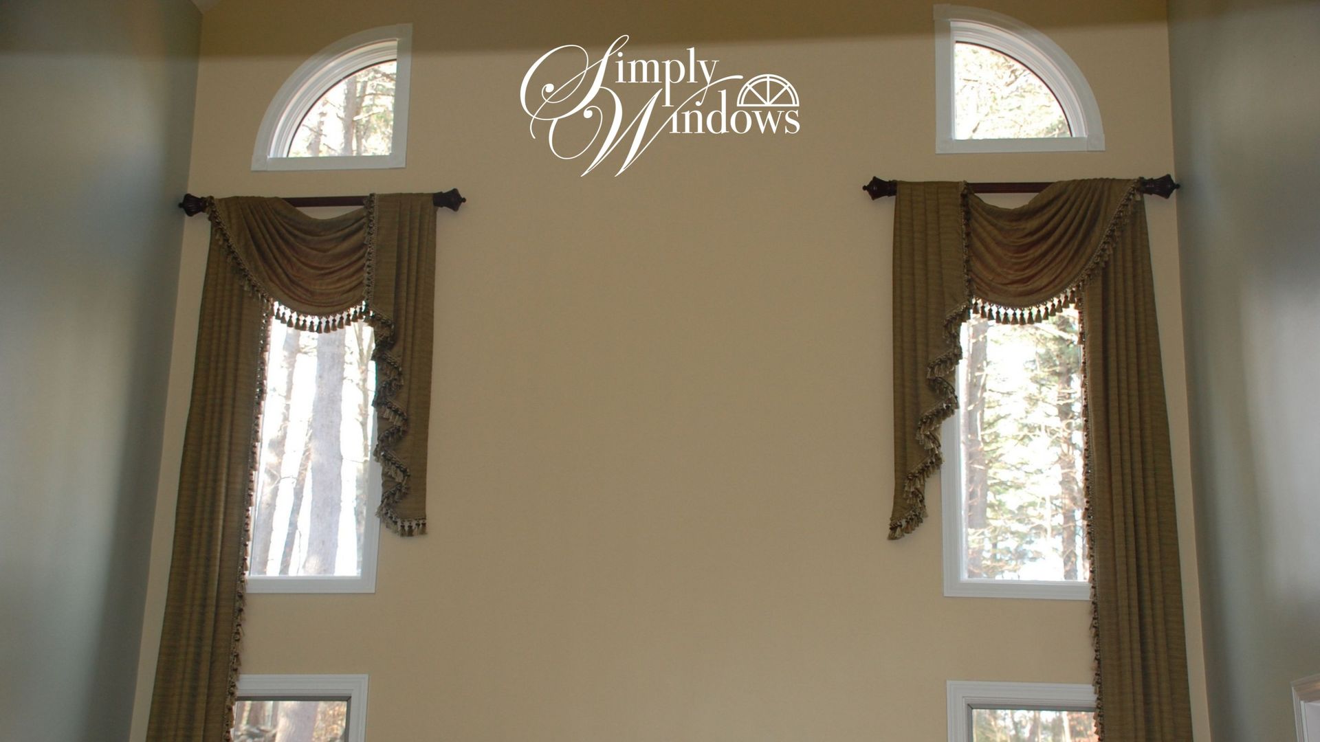 Curtained windows on a beige wall with a “Simply Windows” sign centered above them